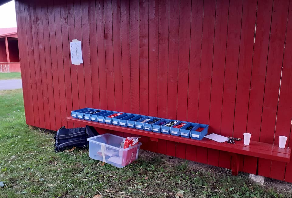 En række af kasser med mærker i ligger på en bænk. Ved siden af hænger en prisliste.